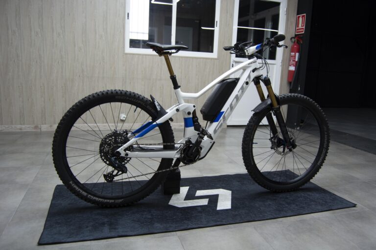 Bicicleta eléctrica blanca y azul sobre alfombrilla en el taller