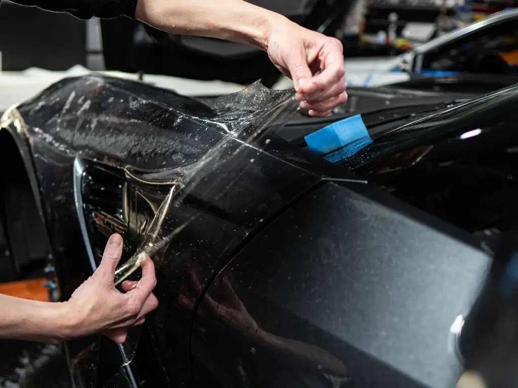 Instalador alisando lámina de PPF con rasqueta sobre un coche negro