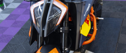 Frontal de moto KTM naranja y negra con protectores naranjas, sobre suelo morado